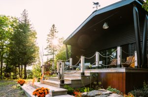 Chalet moderne avec terrasse entouré de verdure, toit courbé, mobilier extérieur et fleurs orange vives